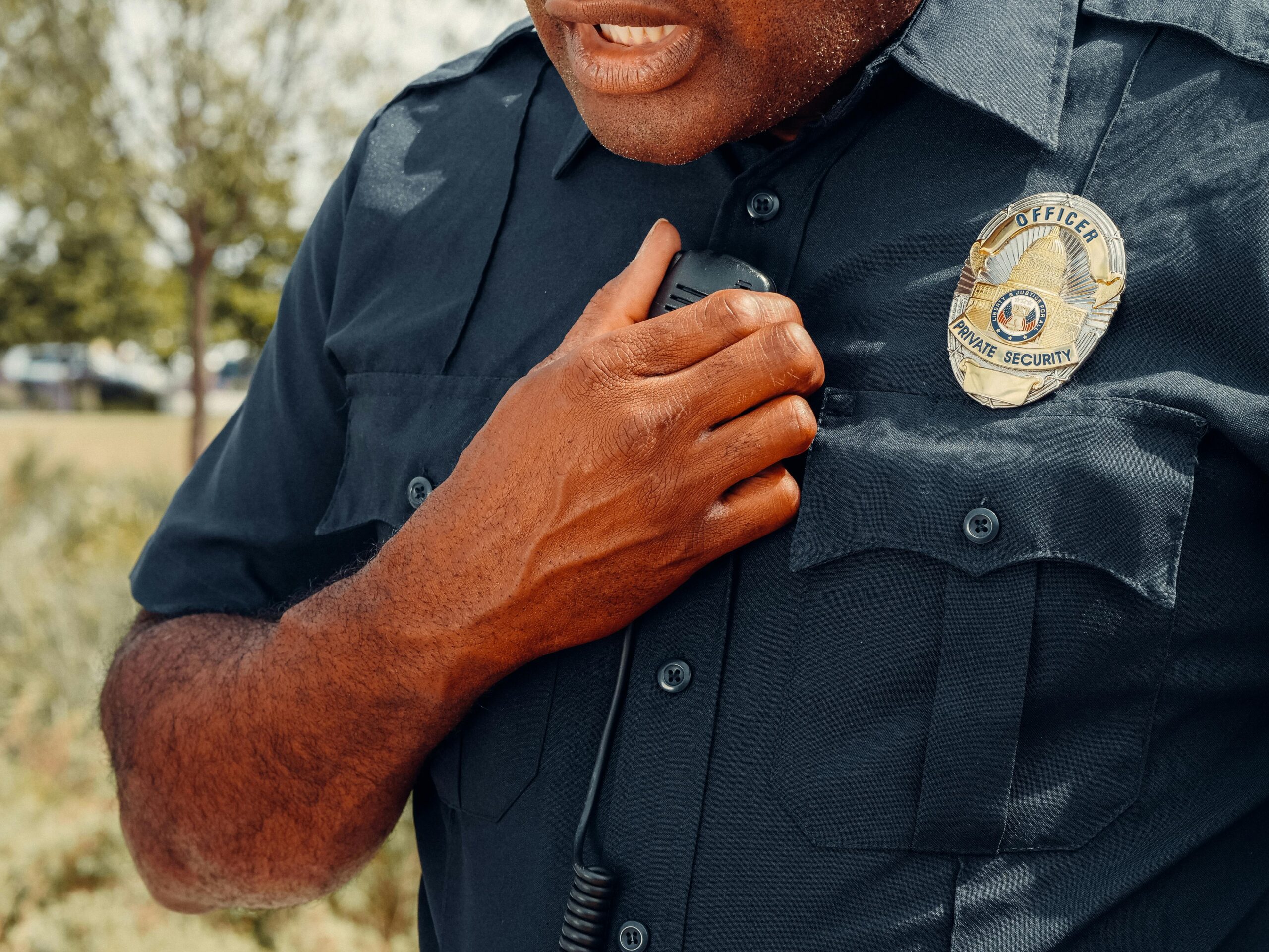 About Us Close-up of a security officer using a radio outdoors, showcasing professional security attire.